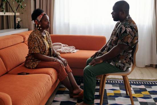 A husband and wife having a conversation as they sit across from each other in their living room.