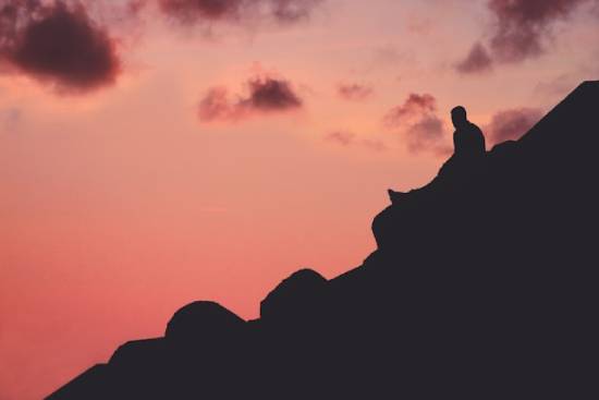A Man Resting On a Peak A silhouette of a man resting on a mountain peak before continuing with his goal of climbing to the top.