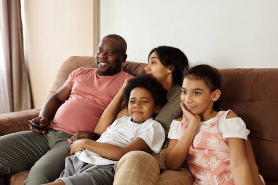 Happy family sitting on a couch watching an educative TV program and enjoying each other's company.