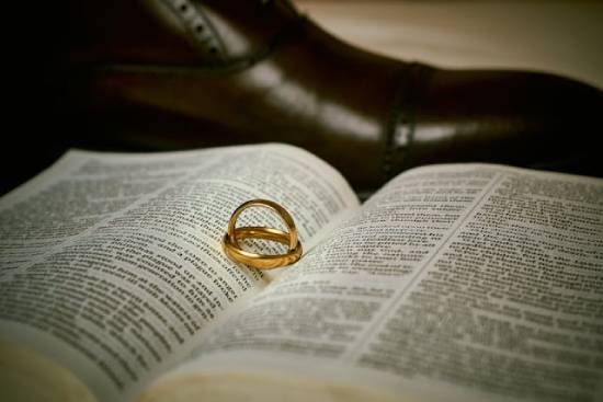 Golden wedding rings placed inside an open Bible next to a black leather shoe.
