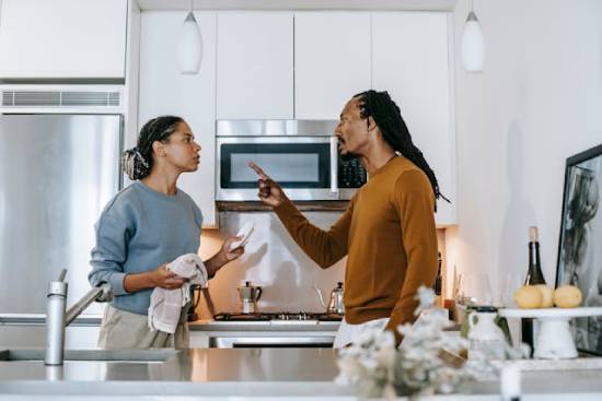 An angry man threatening his wife during an aruguemnt in the kitchen.