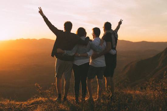 A group of teenagers watching the sunset from a mountaintop.