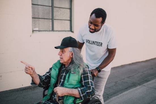A gentleman in white T-shirt volunteering to help move an old lady with her wheelchair.
