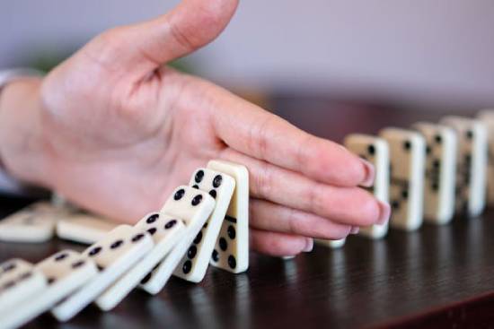 A hand blocking dominoes representing barriers to decisions.