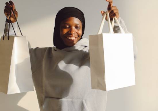 A happy woman in a grey hoodie lifting two gift bags.