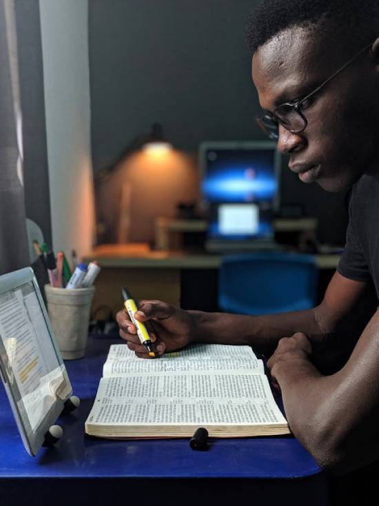 A man keenly studying the bible and marking out texts with a highlighter.