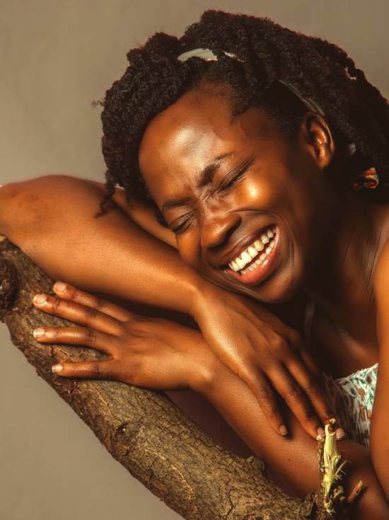 A happy, contented woman smiling while leaning on a tree trunk.
