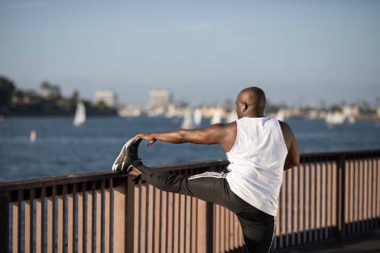 A bald man stretching his legs over metallic rails by the seashore.
