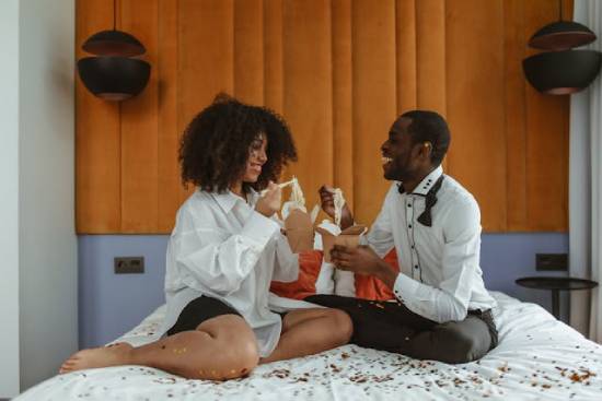 A Couple Snacking in the Bedroom A happy couple eating snacks in the bedroom as they engage in a conversation.