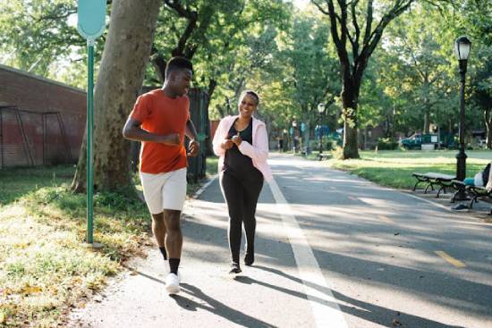 A man a red t-shirt and white shorts and a woman in black and pink jumper running at the park.