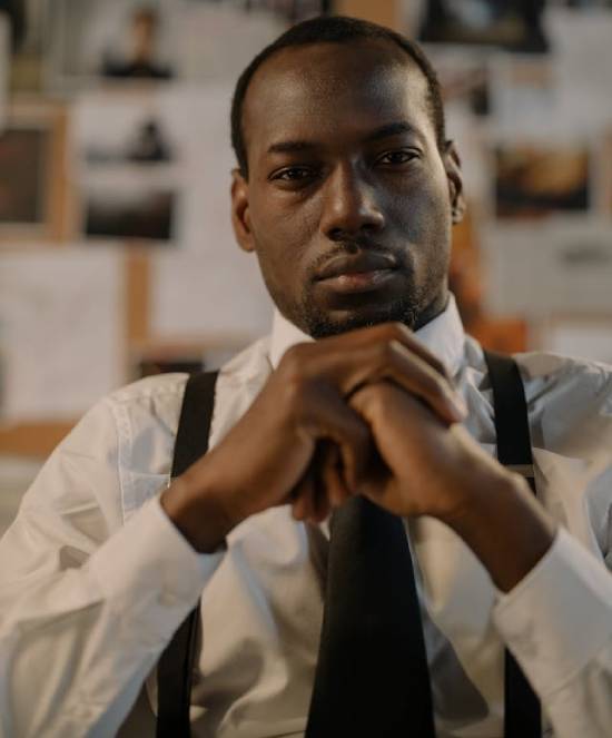 A man depressed in a white shirt, tie and suspenders in deep reflcetions on his desk.