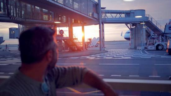 A Man Sitting on a Bench in the Airport A man sitting on a bench and lost in deep thoughts in the Airport at sunset.