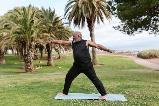 A man dressed in black trauser and top stretching in a park by the seashore.