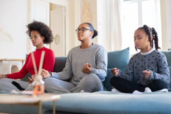 A mother an dtwo daughters practicing mindful meditation on a couch.