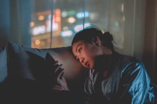 A tired woman using a mobile phone late in the night in a dimly lit room.