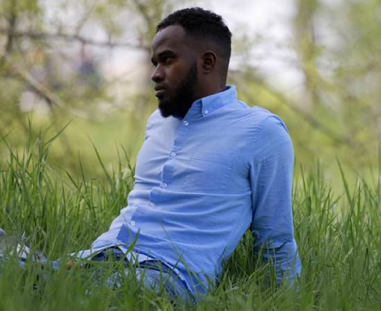 A man in a powder-blue shirt resting in a lush-green grass in a park.