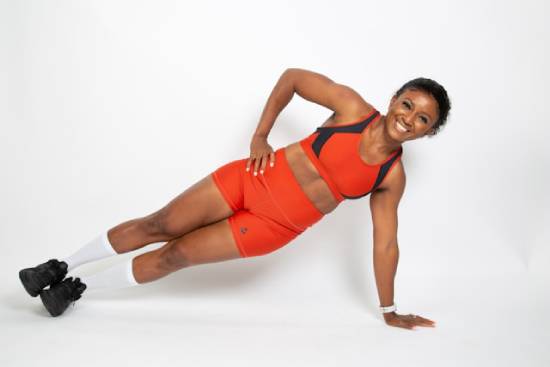 A woman in an orange fitness gear doing a side plank.
