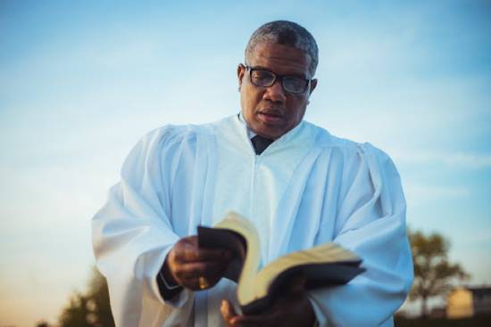 Clergyman Opening the Bible A clergyman opening the Bible in eyeglasses and white sacerdotal robe opening the bible.
