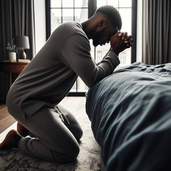A Man Kneeling in Prayer A man in grey sweatsuit kneeling in prayer beside a bed.