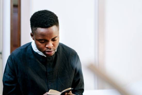 A close-up shot of a man in black sacerdotal robe reading the Bible.