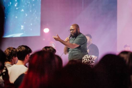 A pastor in jungle-green t-shirt preaching before a congregation.