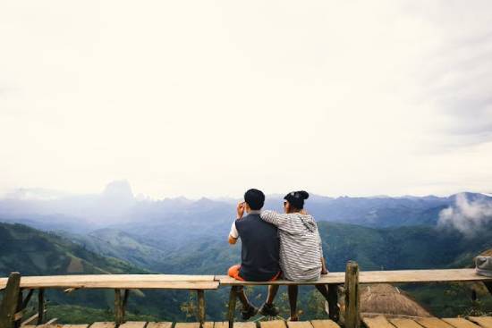 A couple sitting on a bench on a mountaintop and enjoying a beautiful view.
