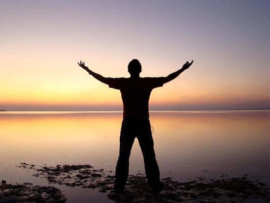 Silhouette of a Man With Oustreched Arms Praying Silhouette of a man with outstretched arms praying by the beach at dusk