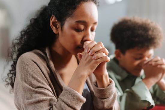  A young woman in a black sweater praying with a friend.