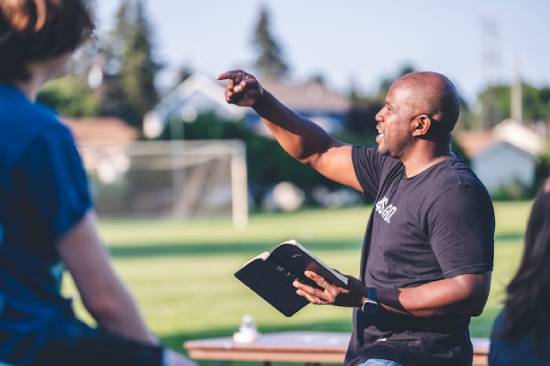 A Man Preaching Outdoors A man in a black T-shirt preaching outdoors to an eager audince while holding an open Bible.