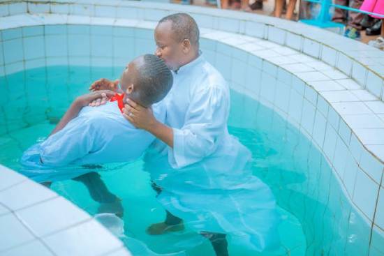 Baptism in a Pool A man dressed in white being baptized in a swimming pool by a clergy wearing white robe.