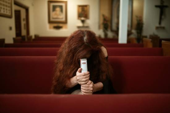A Woman Praying A woman holding her Bible and praying with head bowed while sitting alone on a red pew.