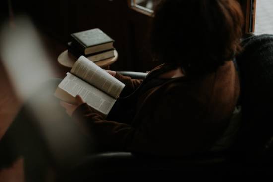 Personal Bible Study A woman with multiple versions of the Bible doing her personal Bible study while sitting on a sofa.