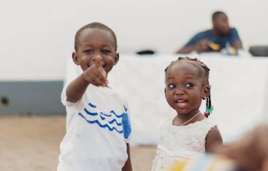 A boy in a white shirt with blue strips standing next to a girl in a white dress.