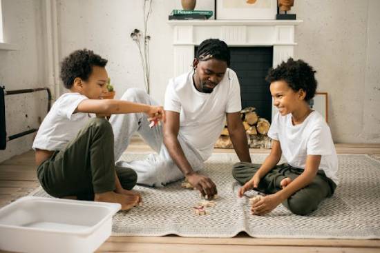 A father and sons  in white tops playing on the floor at home.