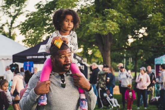 A dad carrying a daughter on his shoulders during a fun activity with families and friends.