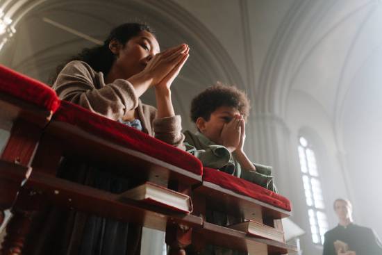 Mother and Son Praying A mother and a son kneeling down praying behind a pew.