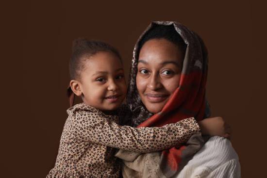A mother in hijab carrying her daughter and smiling to the camera.