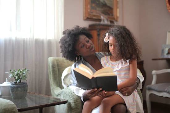 Mother carrying her daughter on her lap and reading to her Scripture affirmations to remind her of her identity.
