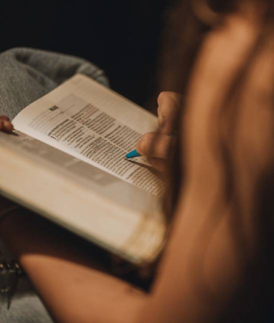 A person having a personal Bible study while holding a green pen and pointing to the Bible.