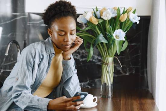 A glowing young woman in a grey top and a denim jacket browsing using her cellphone.