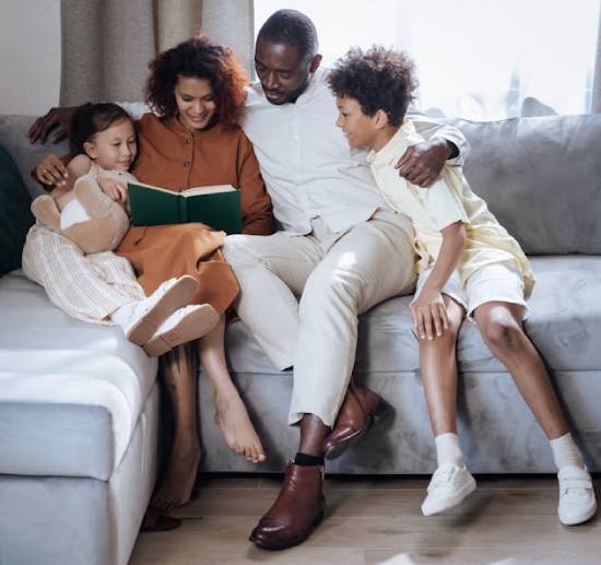 A family of father, mom, and two kids reading a green-covered devotional book together in the living room.