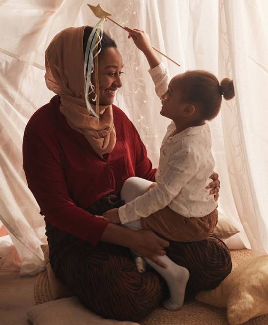A smiling happy girl sitting on the lap of her mother showing her a toy.