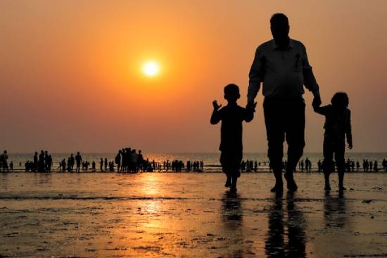 Silhouette of a father walking his two kids to a families day out by the beach.