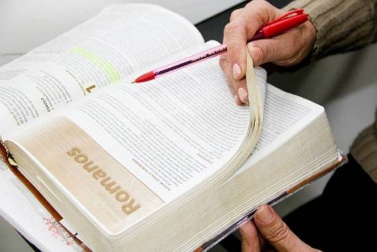 Upclose photo of a person reading the Bible and carryingba red pen.