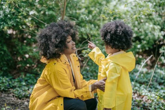 A woman in a yellow jacket squating to talk a kid equally wearing a yellow jacket on level height.