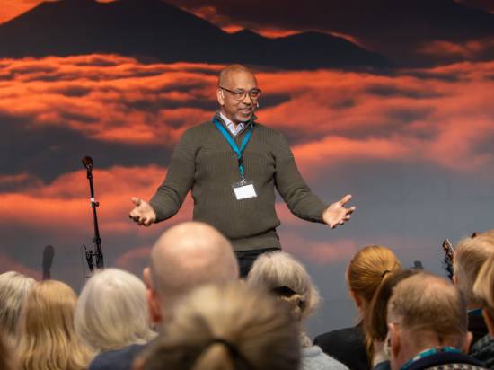 A pastor in spectacles and sweater giving a presentation before an audience.