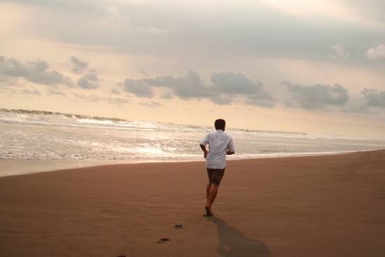 A man in a white shirt and black shorts doing runs by the seashore.