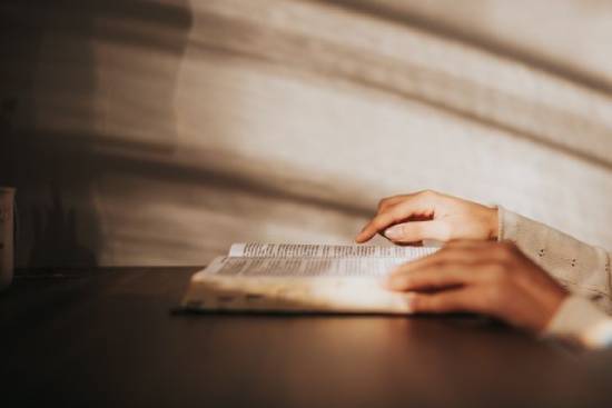 A close-up hands of a person tracing Bible text with index figer while reading the Bible.