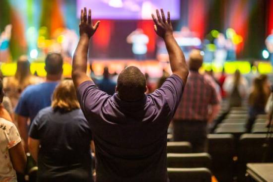 A man lifting both arms in prayer during a church service.