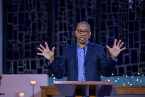 A pastor in a sky blue shirt and navy blue suit leading a bible study on perseverance and endurance.